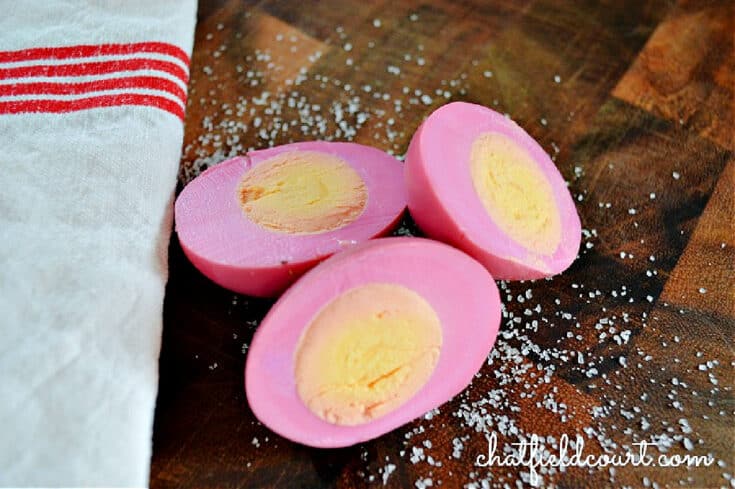 3 pickled eggs sitting in salt on cutting board