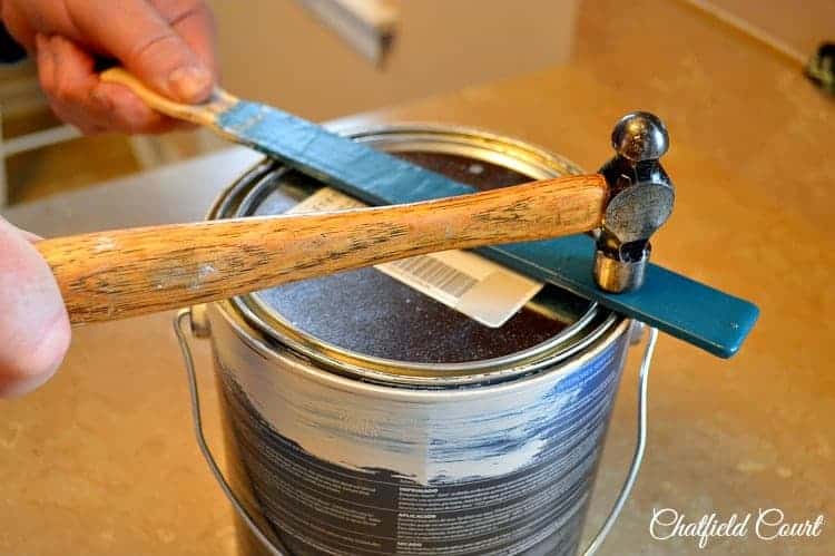 using a hammer to hit a paint stick to close a paint can