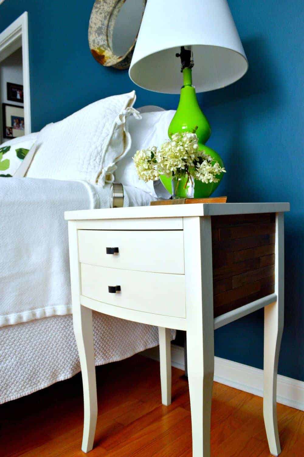 A DIY nightstand with stained wood sticks on the side next to a bed