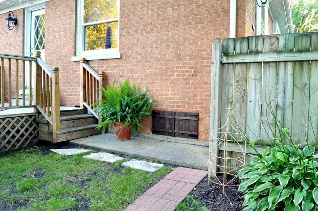 view of DIY window shutter on brick house basement window and a large planted fern next to it