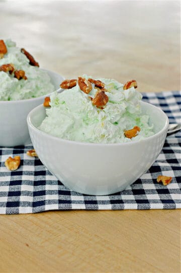green stuff with walnuts on top in a small white bowl