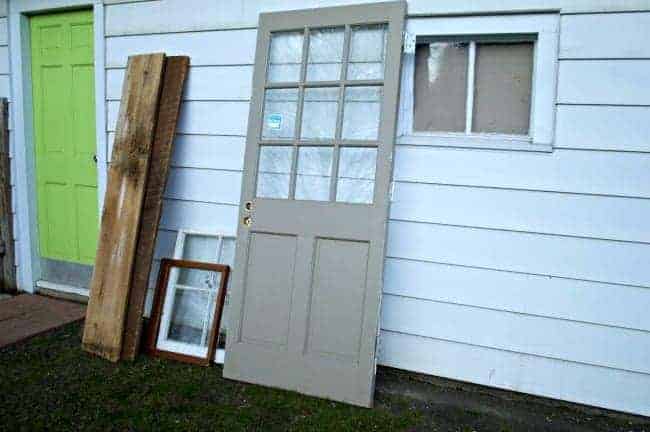 an old door, 2 windows and barn wood leaning against garage