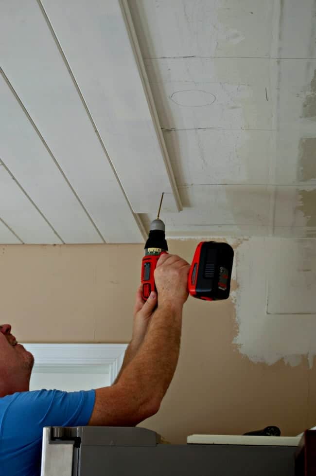 man installing screws in primed tongue and groove ceiling planks in kitchen