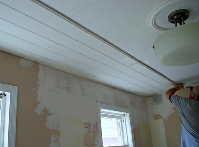 man installing primed tongue and groove ceiling planks in kitchen