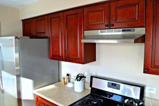 red wood cabinets and stove with hood in small kitchen