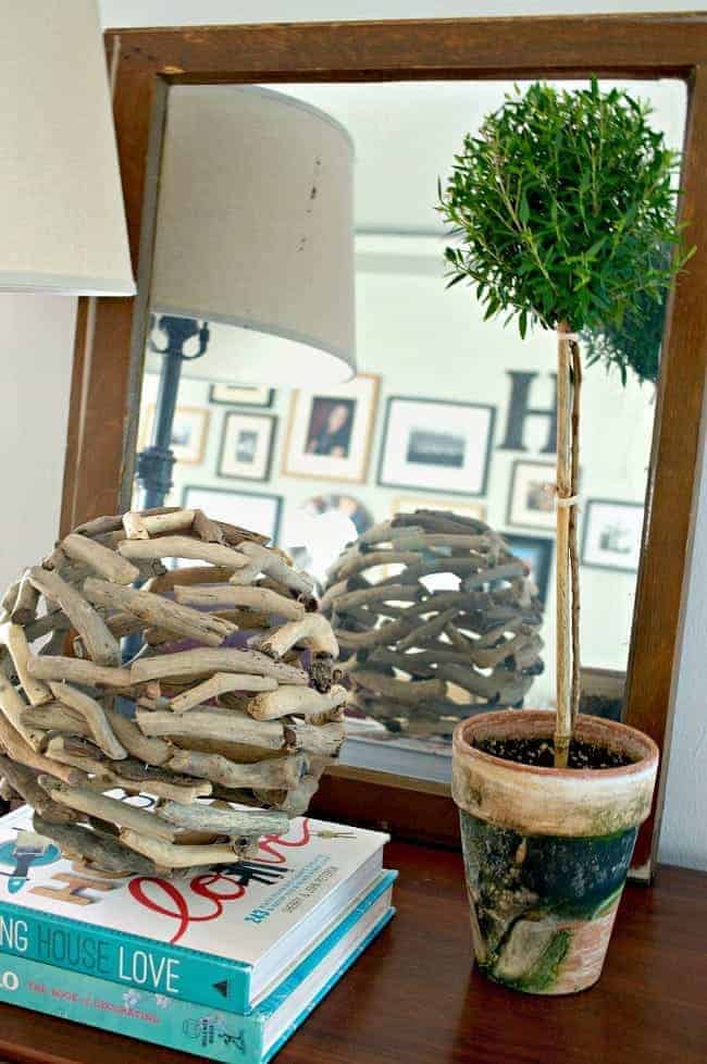 old window turned mirror with a topiary and books on a cabinet