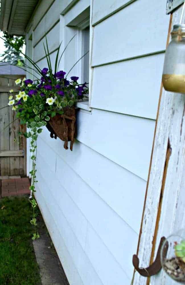 rustic planter box hanging on garage window with petunias and trailing vines