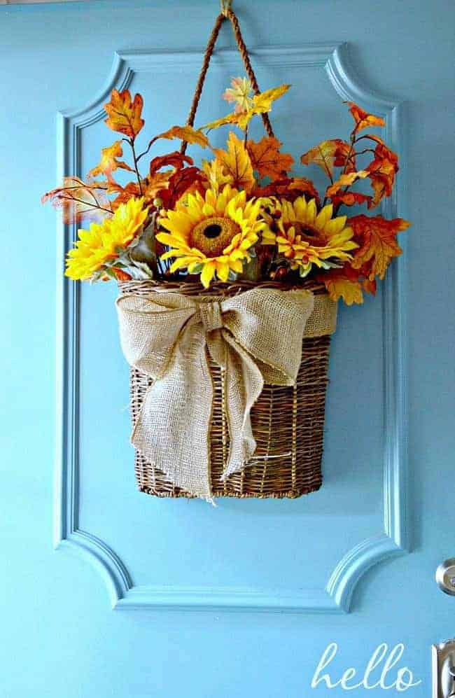 Fall front door basket wreath with burlap bow hanging on a turquoise front door