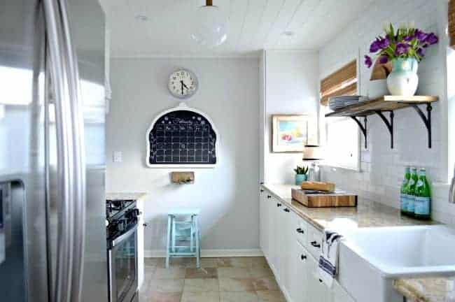 small white galley kitchen with view of chalkboard on wall and kitchen clock