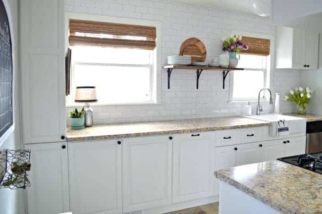 view of white painted kitchen cabinets and granite countertop with 2 kitchen windows with woven shades