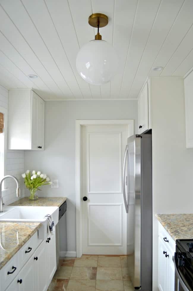 view of white galley kitchen with tongue and groove ceiling, pendant light and gray painted wall