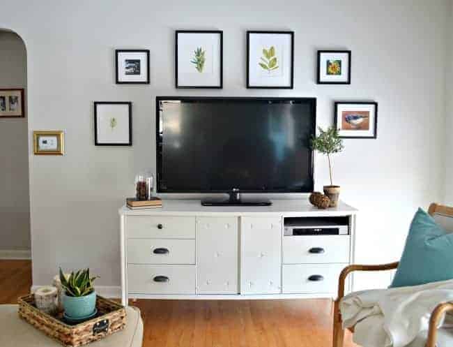 white painted media cabinet with tv and picture frames hanging on the light gray painted wall