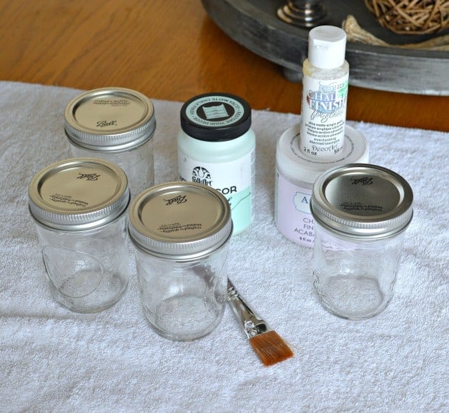 4 small mason jars with lids, chalk paint and craft paint brush on towel