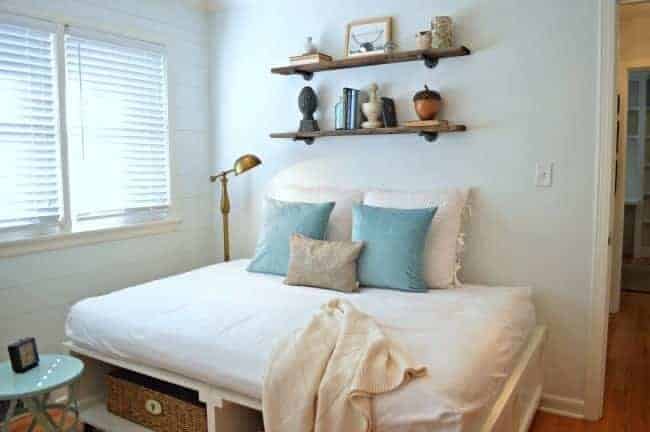 DIY platform bed in guest bedroom with shelves hanging on wall over it