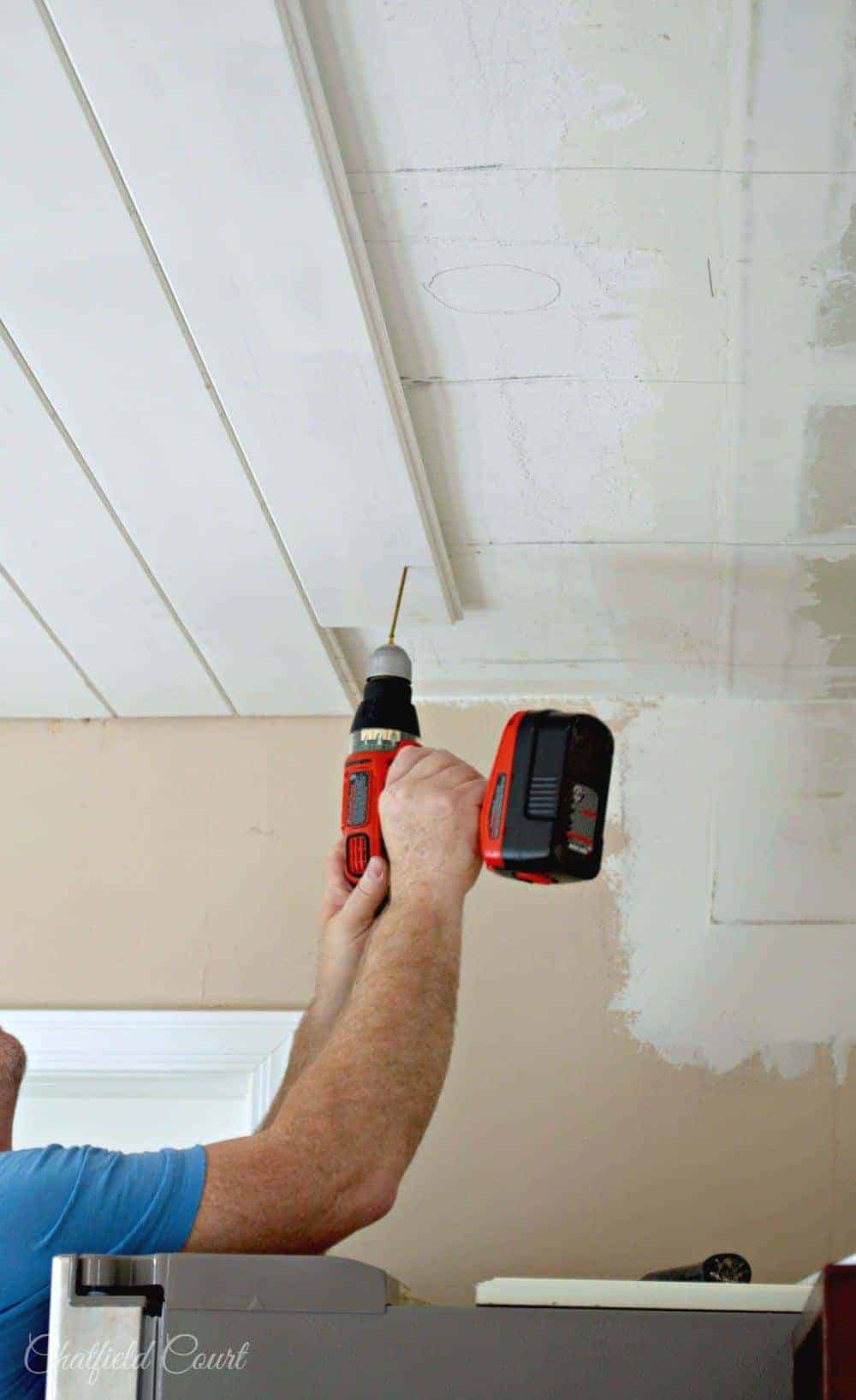 man screwing up tongue and groove plank on ceiling