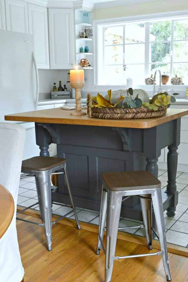 painted kitchen island with a woven tray on top and metal and wood stools