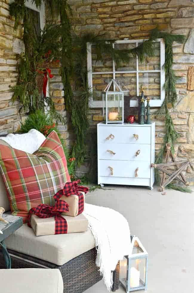 front porch decorated for Christmas with greens around front door and plaid pillow on chair