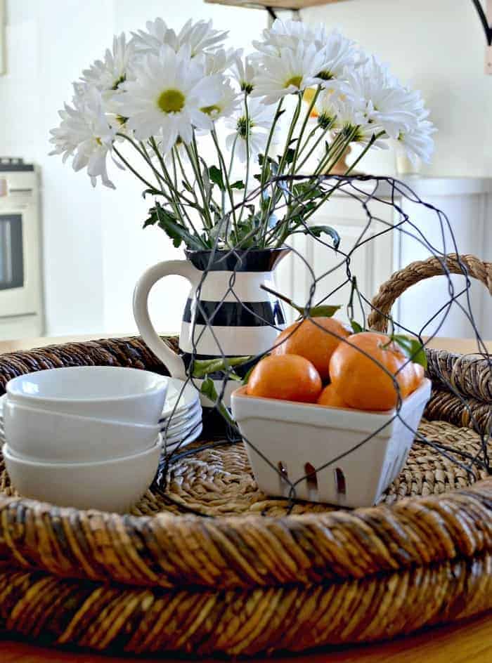 round woven tray with vase of daisies, a bowl of oranges and small white bowls