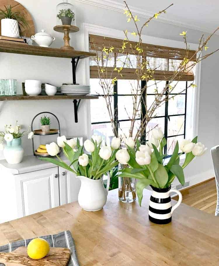 pitchers of white tulips on a kitchen island with black painted window frames behind them