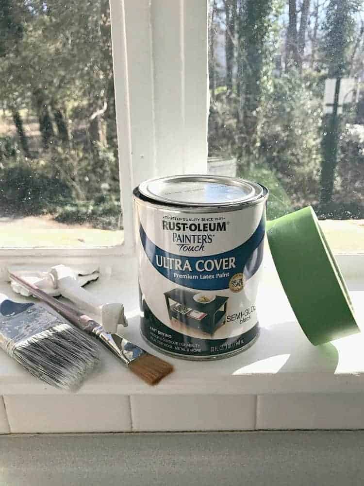 paint can, paint brushes and painter's tape in window to be painted black