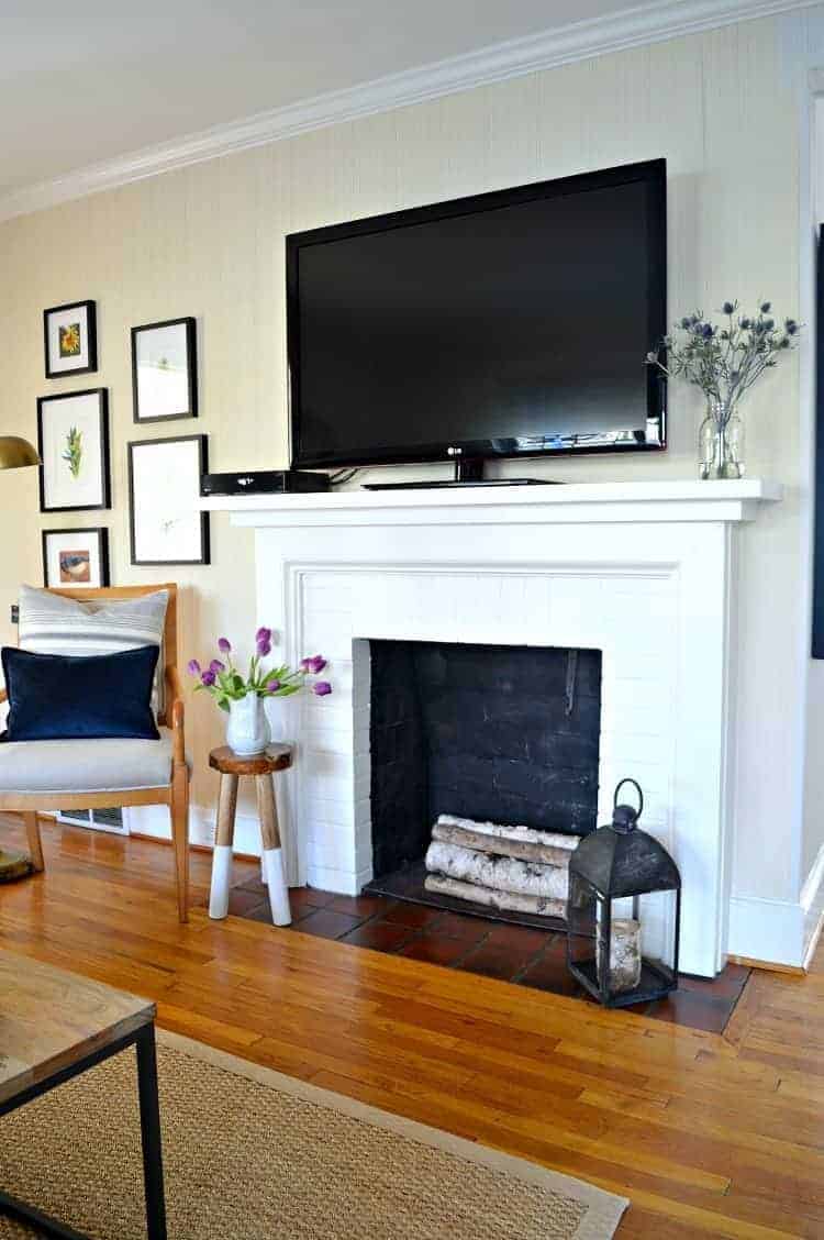 white brick fireplace with tv on mantel and stool with flowers next to it