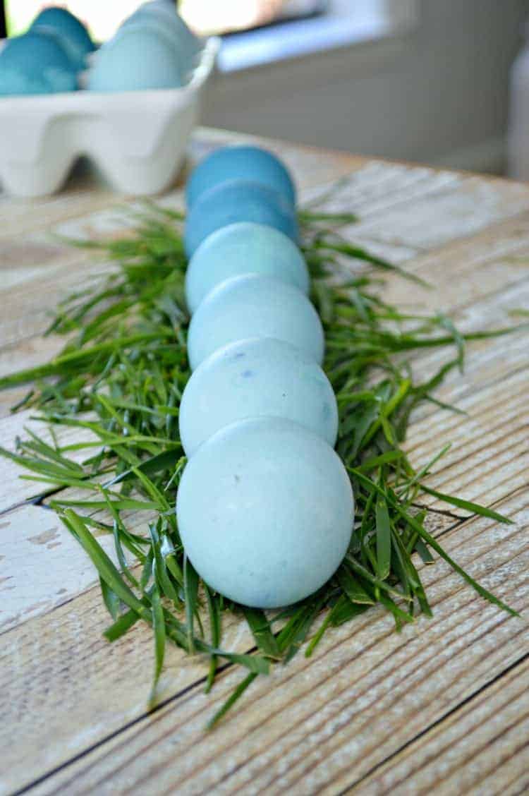 6 naturally dyed Easter eggs in different shades of blue in a row on grass