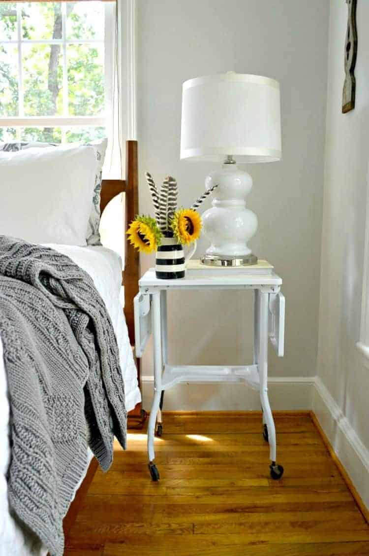 white metal nightstand with lamp and a pitcher of sunflowers