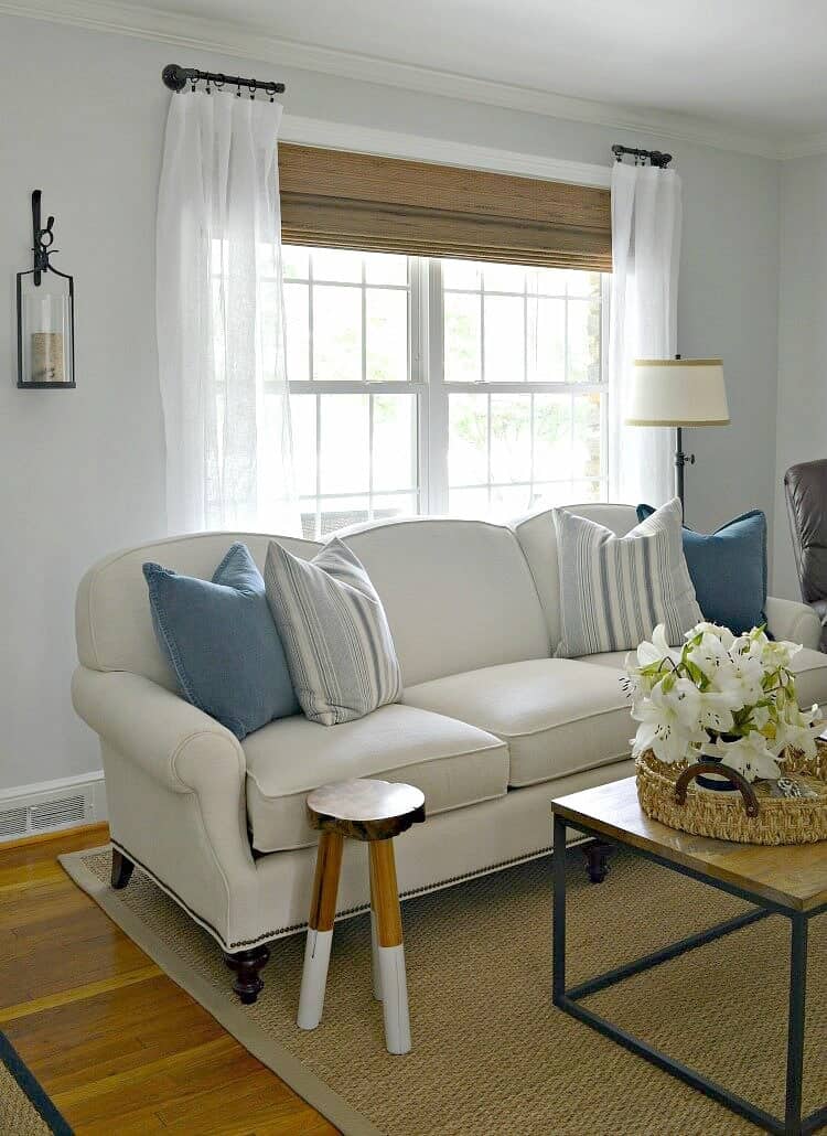 couch in front of living room window with woven shade and white curtains 