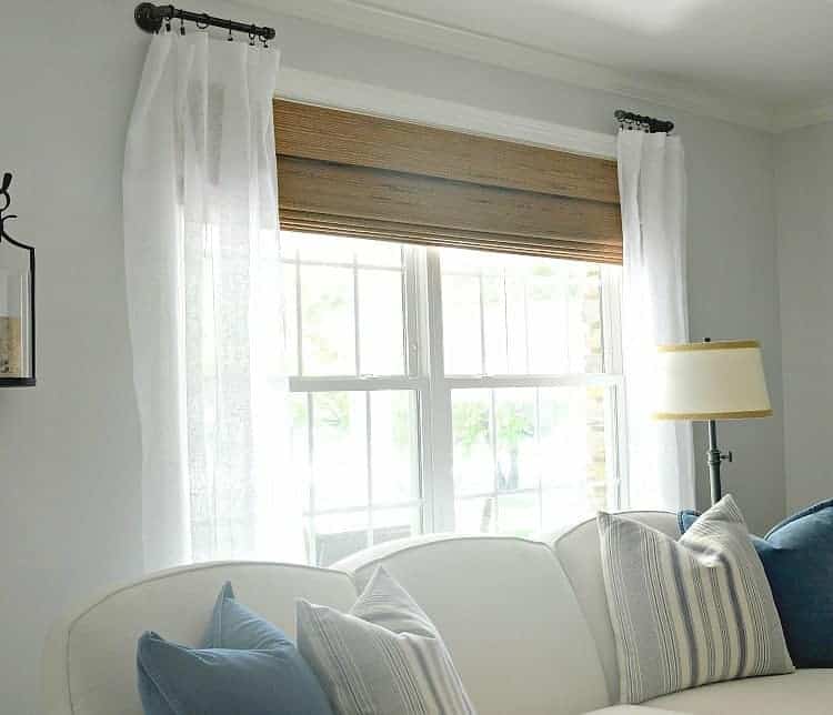 couch in front of living room window with woven shade and white curtains 