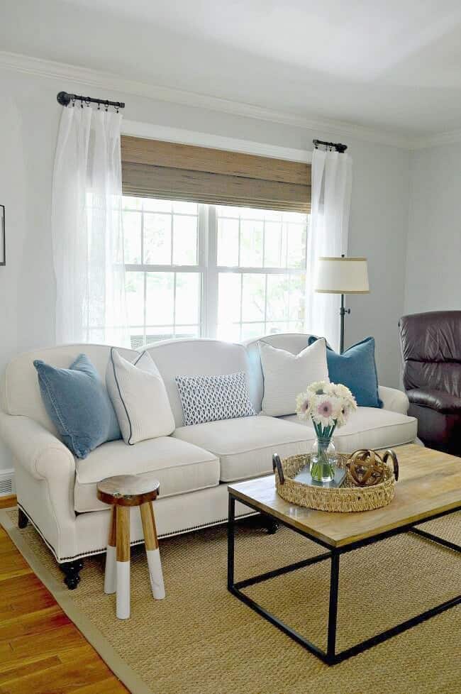 white sofa with blue and white pillows on it and wood and iron coffee table