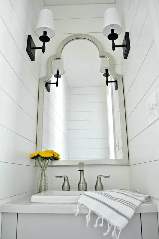 small powder room vanity, mirror and sconces with a striped towel on the vanity and yellow flowers in a glass vase