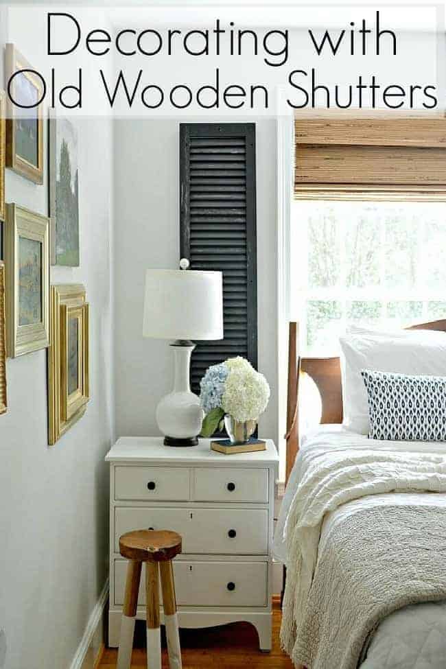 small master bedroom with white nightstand and old wooden shutter on wall next to window