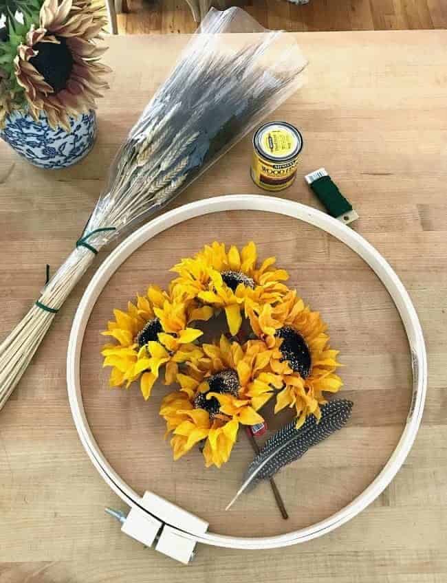 supplies to make fall hoop wreath including an embroidery hoop. can of stain, dried grass, faux sunflowers and feathers