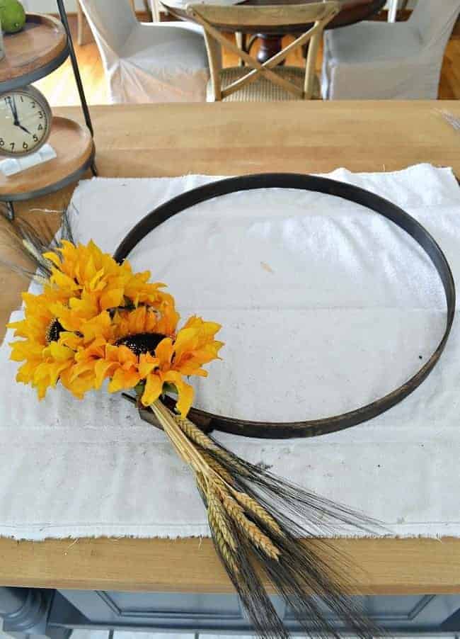 Attaching wheat and sunflowers to an embroidery hoop with floral wire to create a simple DIY fall front door wreath. 