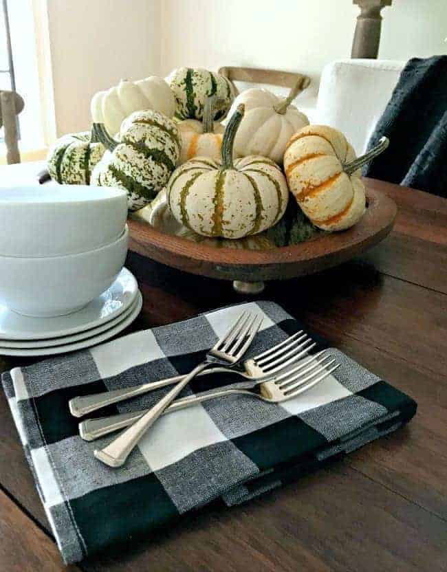 mini pumpkins stacked on top of fall table centerpiece made with a thrifted mirror, with black and white napkins and white dishes