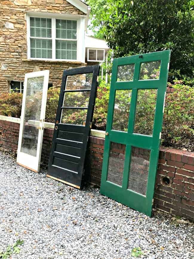 3 thrift store doors leaning against a brick wall. One white, one black and one green.