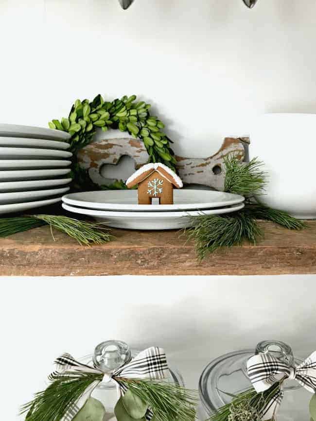 Mini gingerbread cookie house on white plates on shelf.