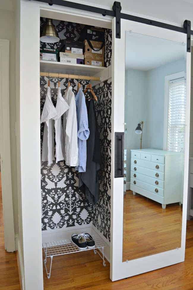 hanging clothes in small closet with wall paper and mirrored barn door