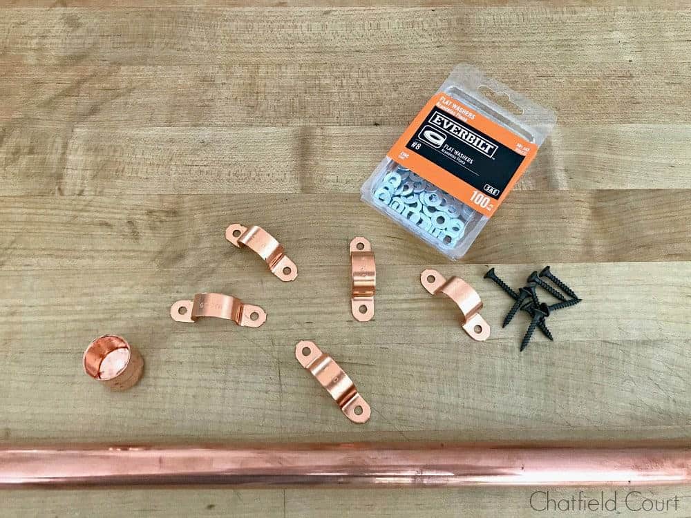 copper pipe, tube straps, end cap, wood screws and a box of washers on a butcher block countertop
