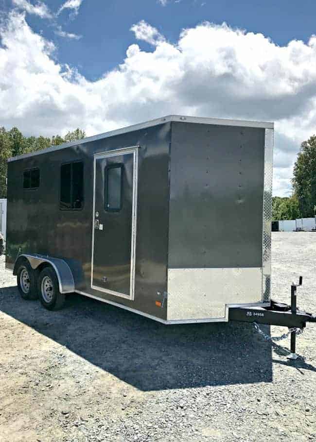 A gray enclosed landscape trailer with 2 windows and a door