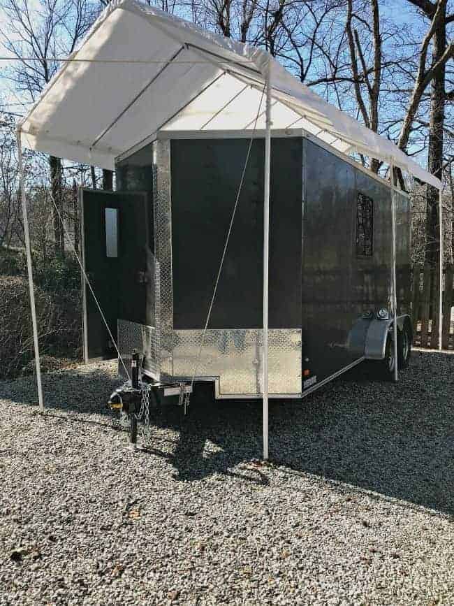 outside view of gray enclosed trailer camper with white awning over it