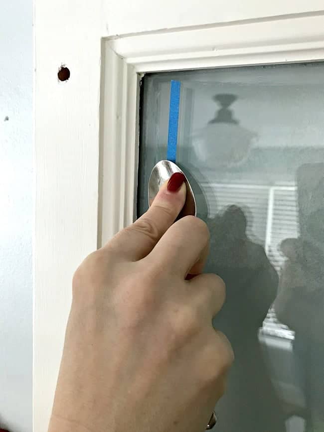 adding painter's tape to a bathroom door window and smoothing it out with a spoon