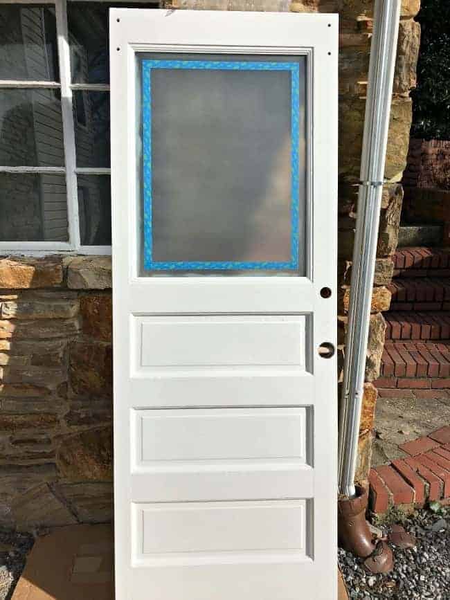 old white door with window taped with painter's tape and frosted 