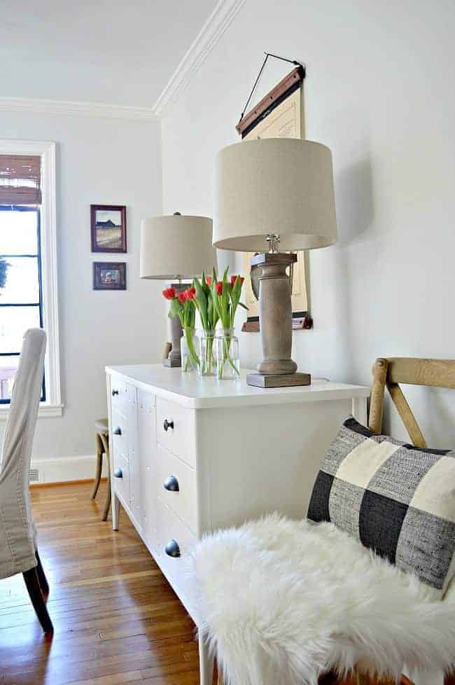 white buffet with 2 lamps and 3 glass bottles and red tulips