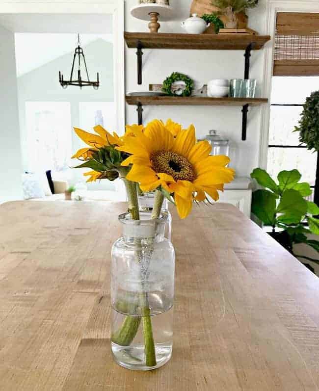 3 glass bottles with sunflowers in them on a kitchen island