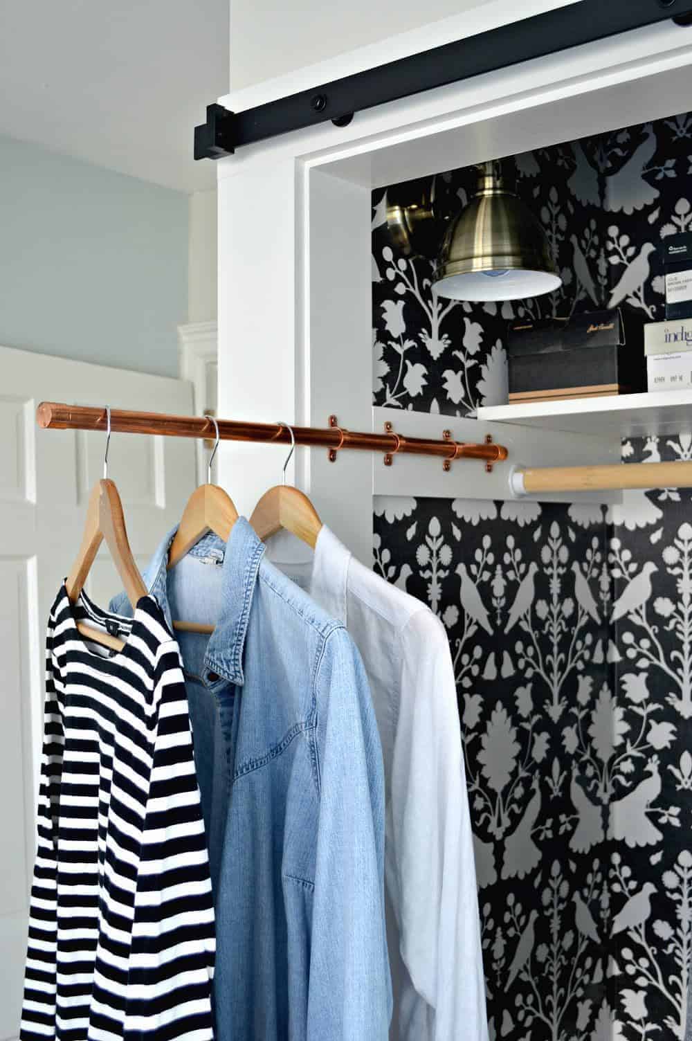 3 shirts hanging on copper pipe sliding clothes rod in small closet with bird wallpaper