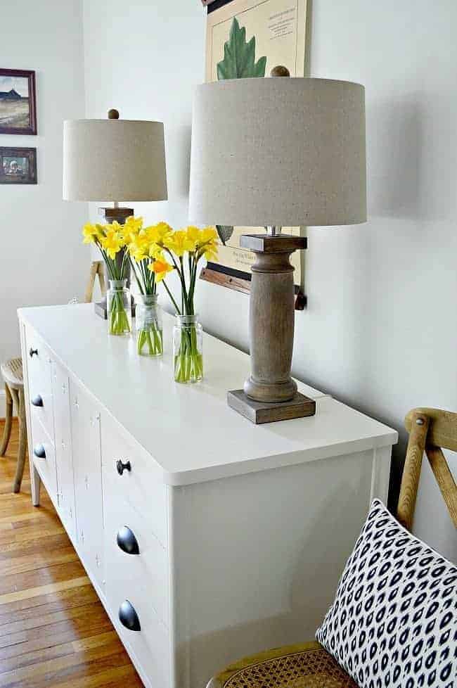 tulips in glass bottles on white painted dresser in a dining room