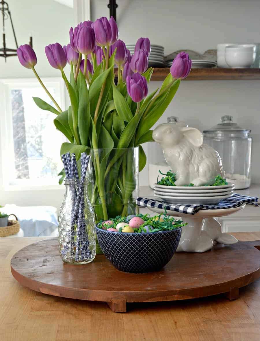 spring vignette with purple tulips, white bunnies, blue straws in a glass bottle and a navy bowl with candy eggs