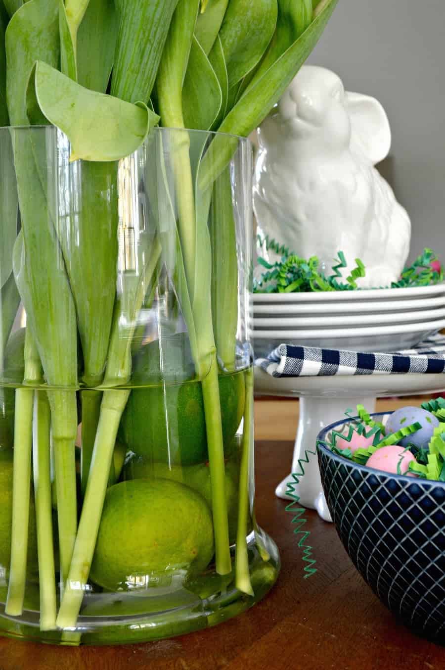 spring vignette with purple tulips in a glass vase with limes, a white bunny and a navy bowl with candy eggs