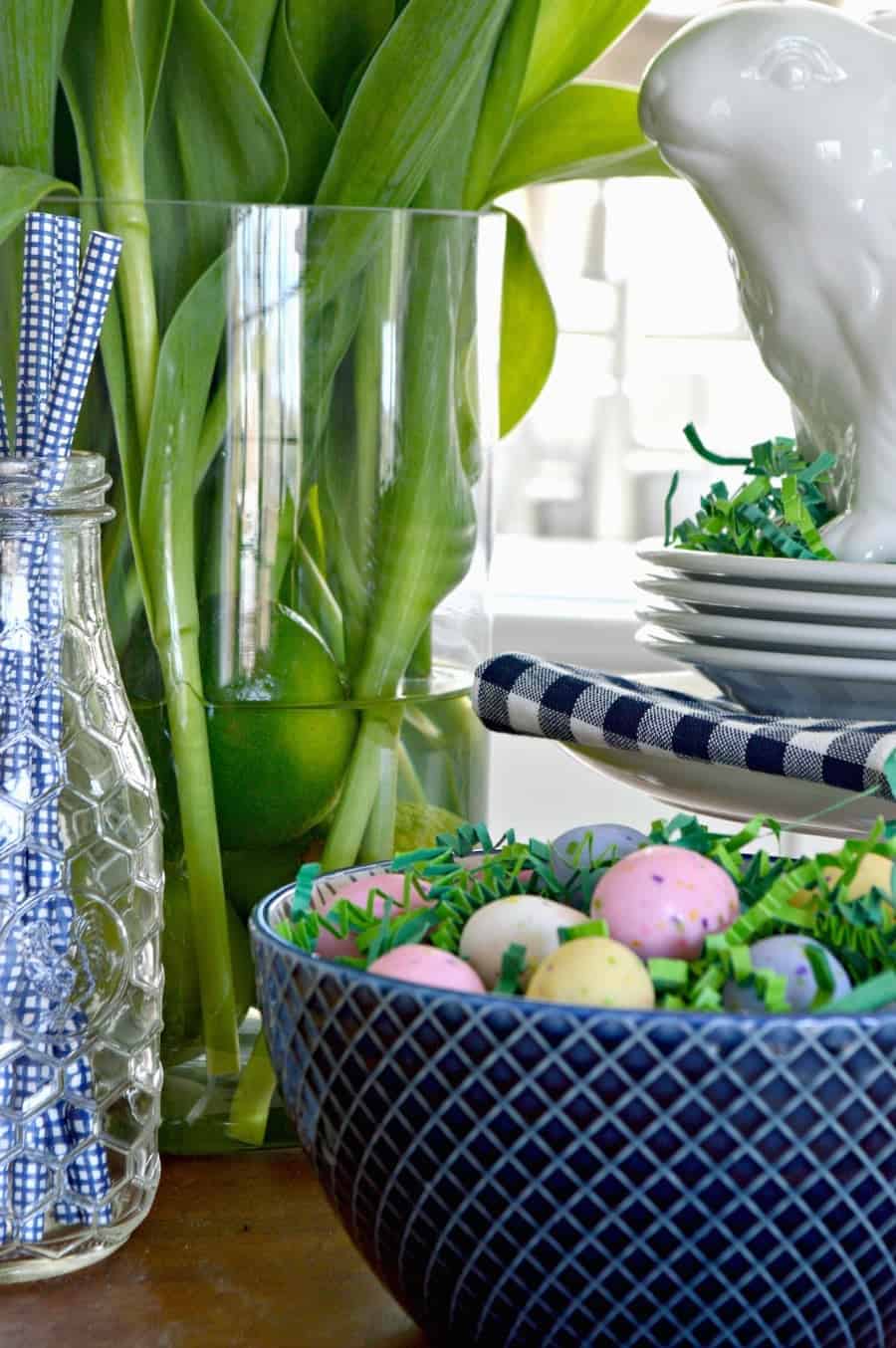 spring vignette with a white bunny, blue straws in a glass bottle and a navy bowl with candy eggs